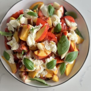 a plate full of colorful tomatoes, peaches, burrata, and basil